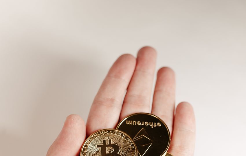A hand holds various cryptocurrency coins including Bitcoin, Ethereum, and others.
