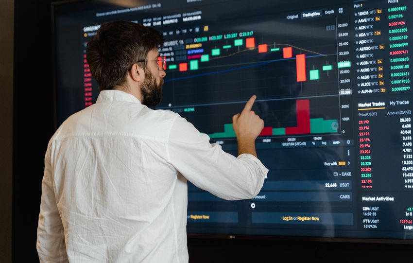 A man analyzes cryptocurrency graphs on a touchscreen monitor in a modern office setting.