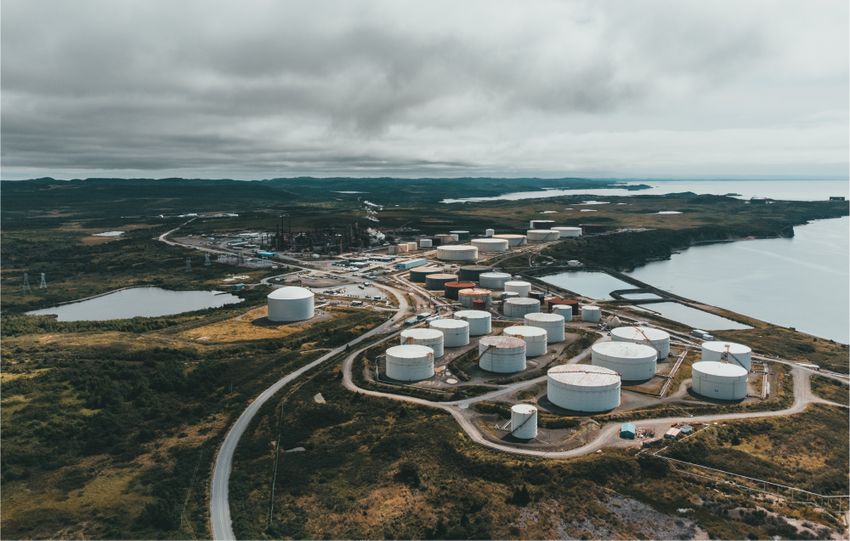 Aerial landscape shot of a coastal oil refinery with storage silos under cloudy skies.