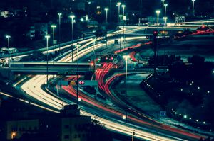 Aerial view of illuminated night-time city highways with dynamic light trails and bustling traffic.