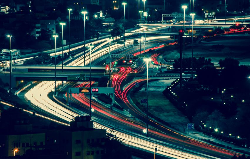 Aerial view of illuminated night-time city highways with dynamic light trails and bustling traffic.