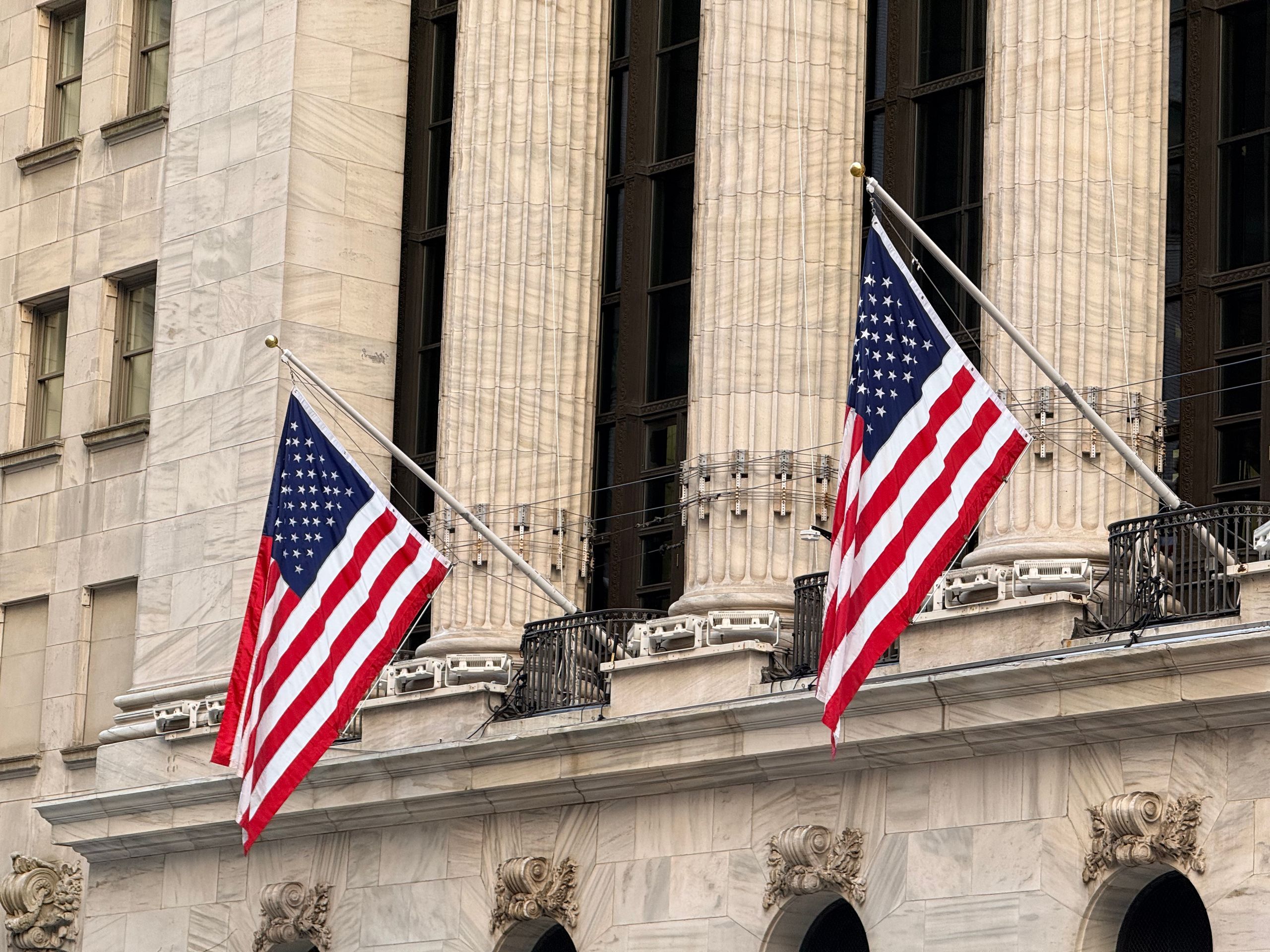 American flags displayed prominently on a historic Wall Street building in New York City.