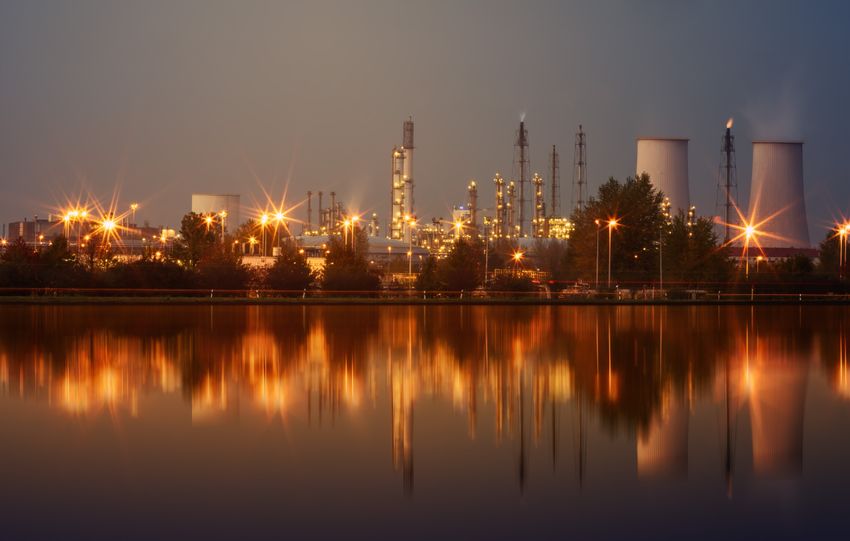 Industrial plant with reflection in water at twilight, showing smoke stacks and lights.