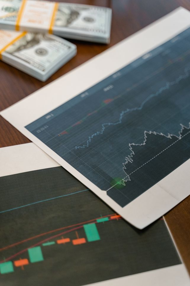 Papers with financial graphs beside stacks of US dollar bills representing market analytics.