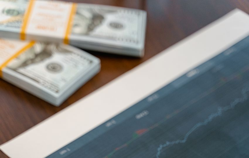Papers with financial graphs beside stacks of US dollar bills representing market analytics.