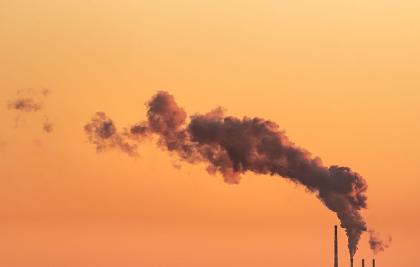 Smoke billowing from industrial chimneys against a vibrant orange sunset sky in Gdańsk, Poland.