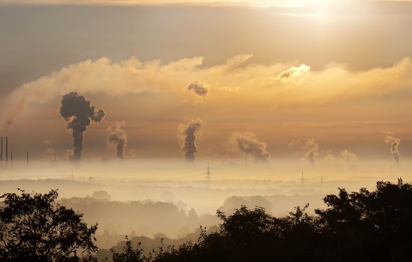 Smoke rising from factory chimneys at sunrise, symbolizing pollution and environmental impact.