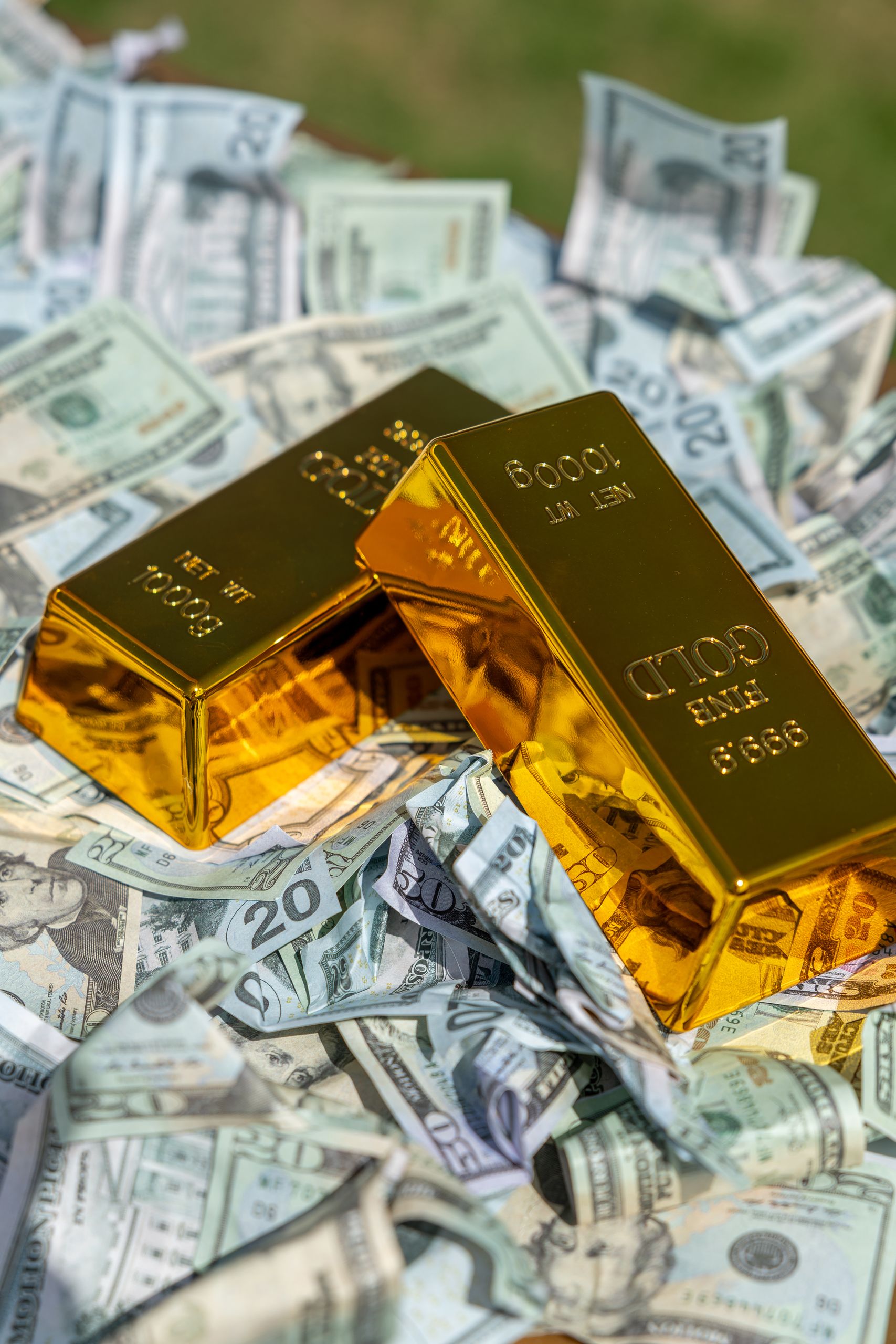 Two gold bars rest on a pile of US dollar bills, symbolizing wealth and prosperity.