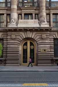 A man walks past the grand entrance of Banco de México, showcasing its classic architecture.