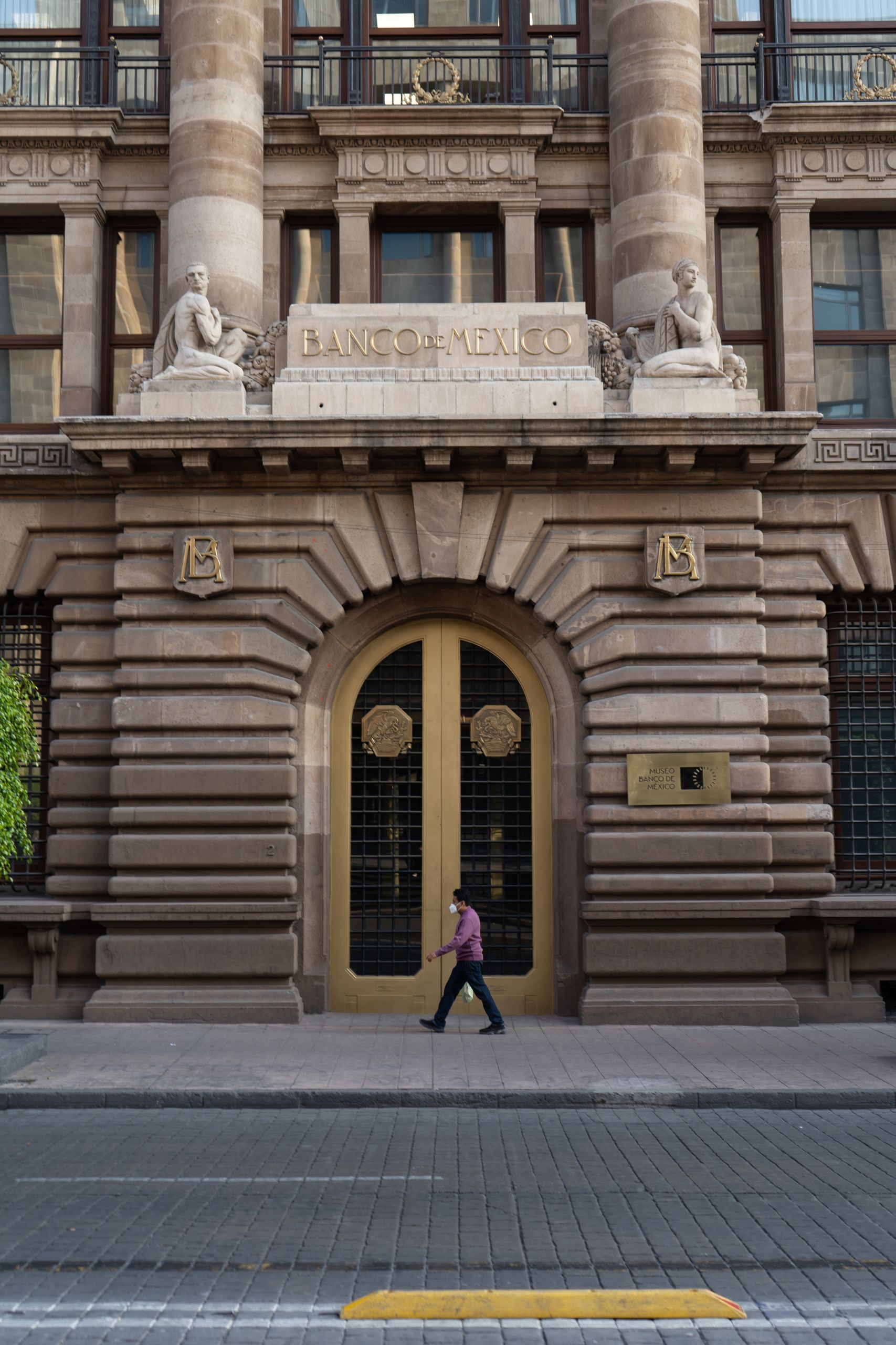 A man walks past the grand entrance of Banco de México, showcasing its classic architecture.
