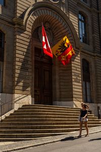 A woman walking by the Palais de Justice in Genève, featuring Swiss and cantonal flags.