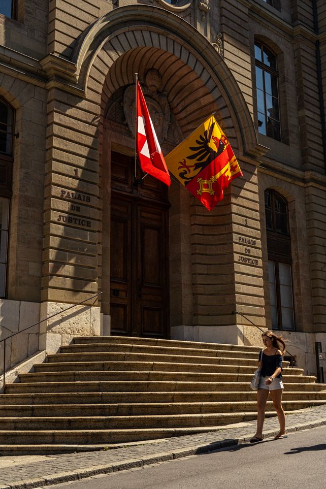 A woman walking by the Palais de Justice in Genève, featuring Swiss and cantonal flags.
