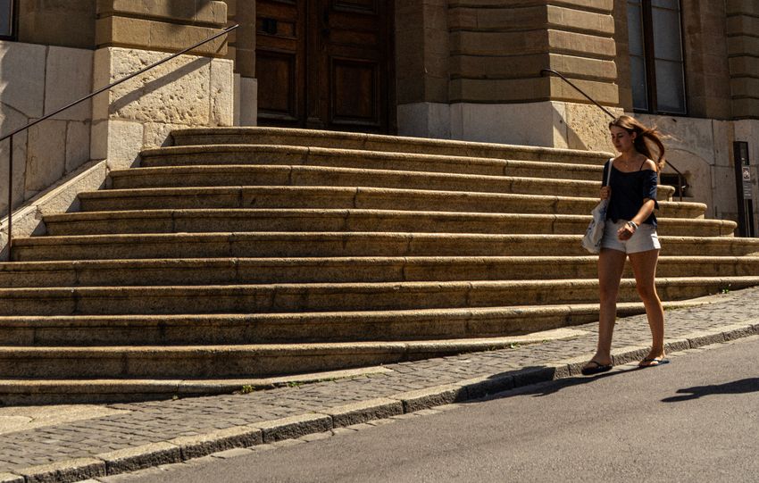A woman walking by the Palais de Justice in Genève, featuring Swiss and cantonal flags.