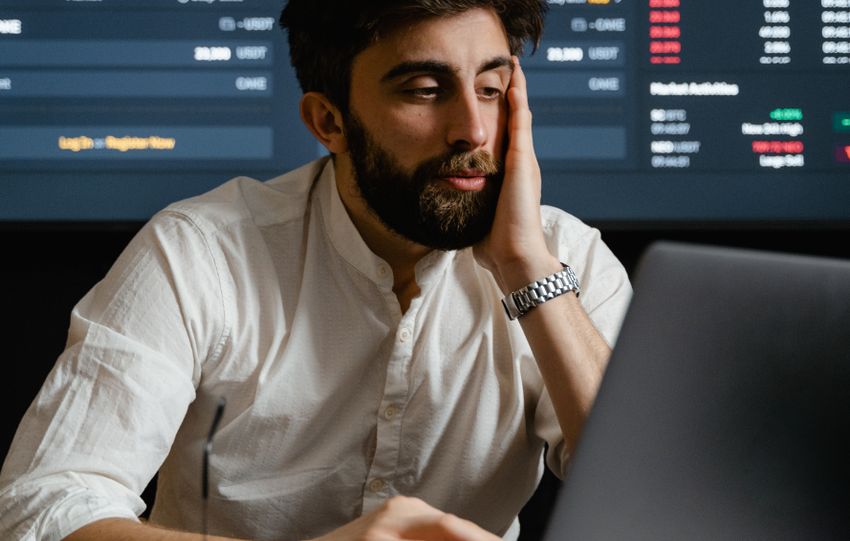 Bearded businessman analyzing financial statistics on a laptop, with stock market graphs in the background.