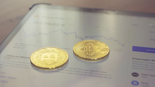 Close-up of two golden Bitcoin coins on a tablet screen displaying financial data.