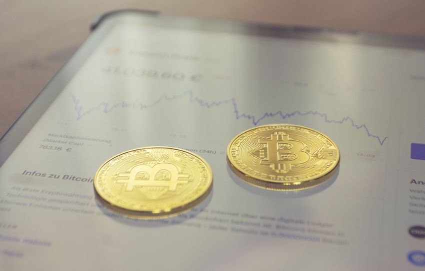 Close-up of two golden Bitcoin coins on a tablet screen displaying financial data.