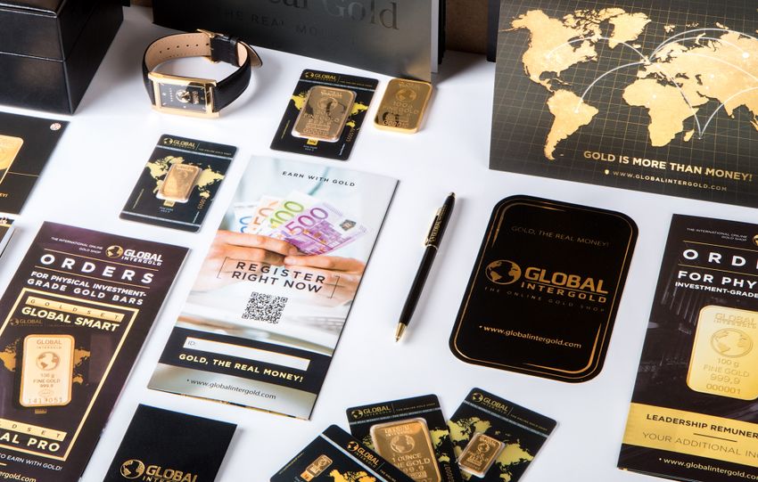 Flat lay of promotional materials for gold investment, featuring brochures, cards, and gold bars.