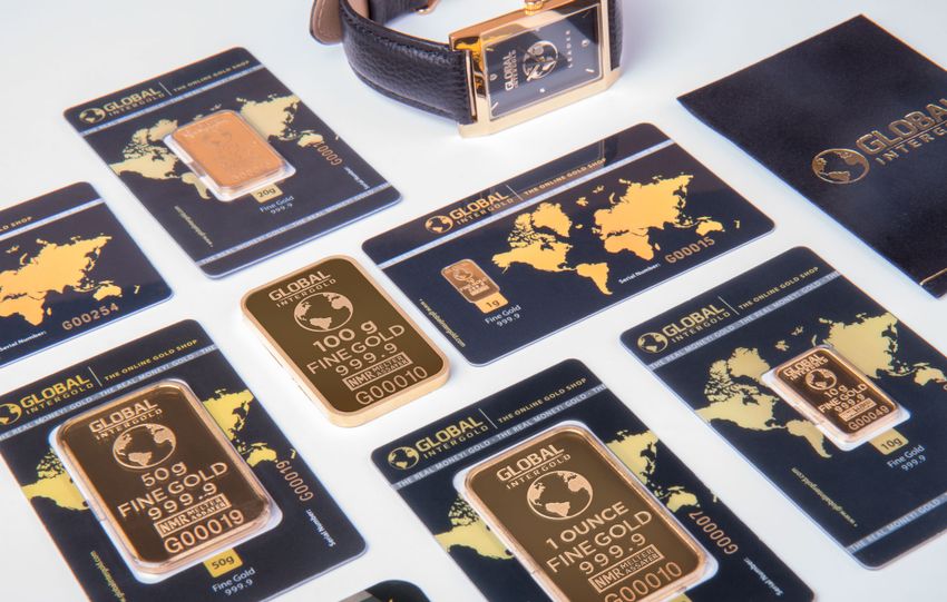 High-angle shot of fine gold bars with a luxury watch and branded packaging.