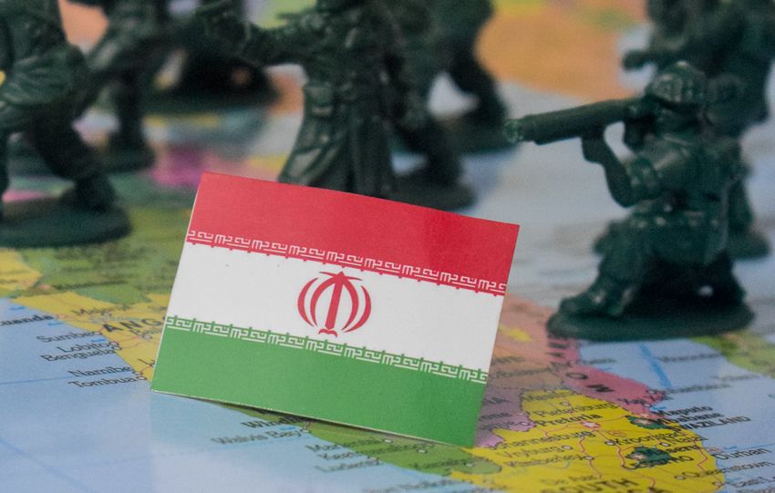 Toy soldiers and Iran flag on a world map symbolizing geopolitical tensions.