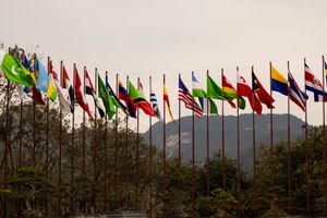 A display of various national flags on flagpoles set against a mountain backdrop, symbolizing global unity.