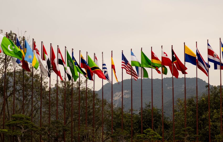 A display of various national flags on flagpoles set against a mountain backdrop, symbolizing global unity.