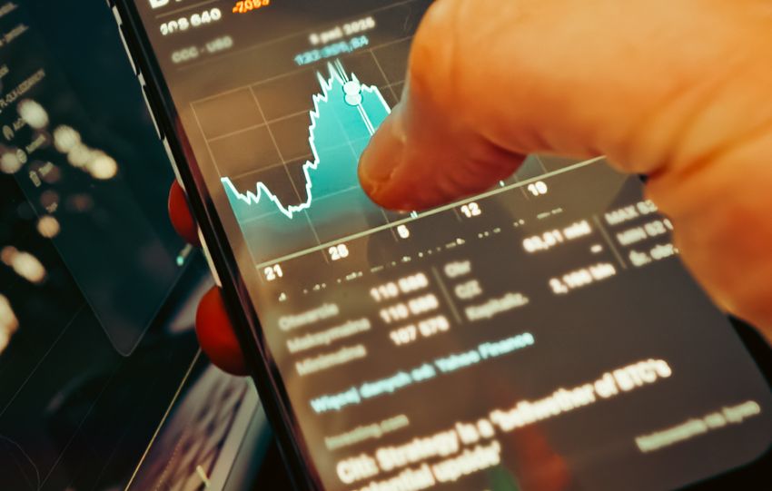 A hand holds a smartphone displaying BTC-USD chart amidst digital trading screens, highlighting crypto finance.