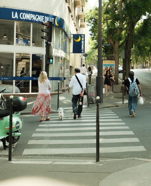 A street scene in Paris with people crossing near La Compagnie Bllu on a warm day.