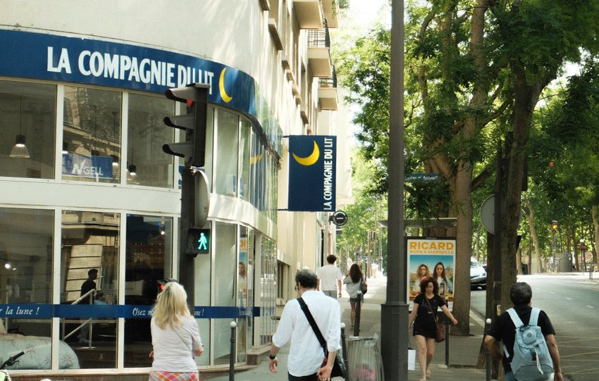 A street scene in Paris with people crossing near La Compagnie Bllu on a warm day.