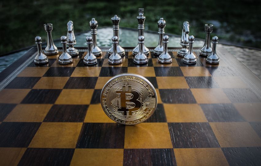 Bitcoin coin standing on a chessboard with silver and brass chess pieces. Concept of strategic digital currency investment.