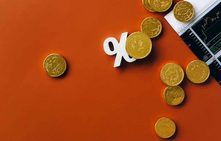 Gold coins scattered with a stock market graph and a percentage symbol on an orange background.