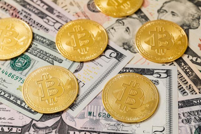 Golden Bitcoin coins scattered over US dollar bills, symbolizing modern digital currency.