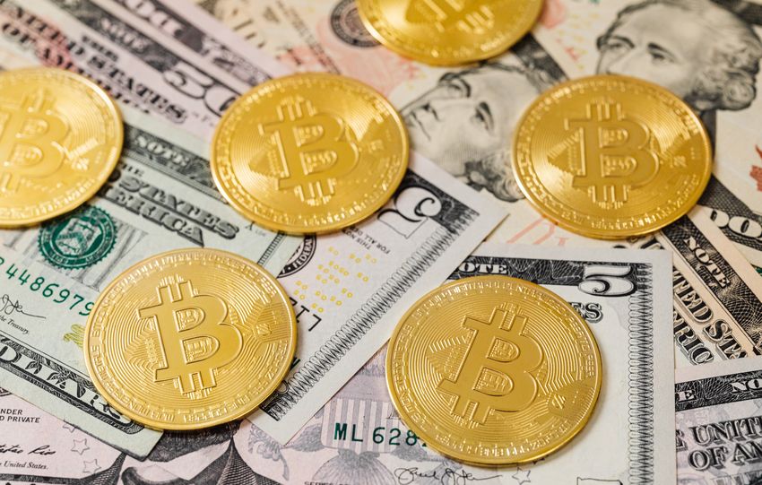 Golden Bitcoin coins scattered over US dollar bills, symbolizing modern digital currency.