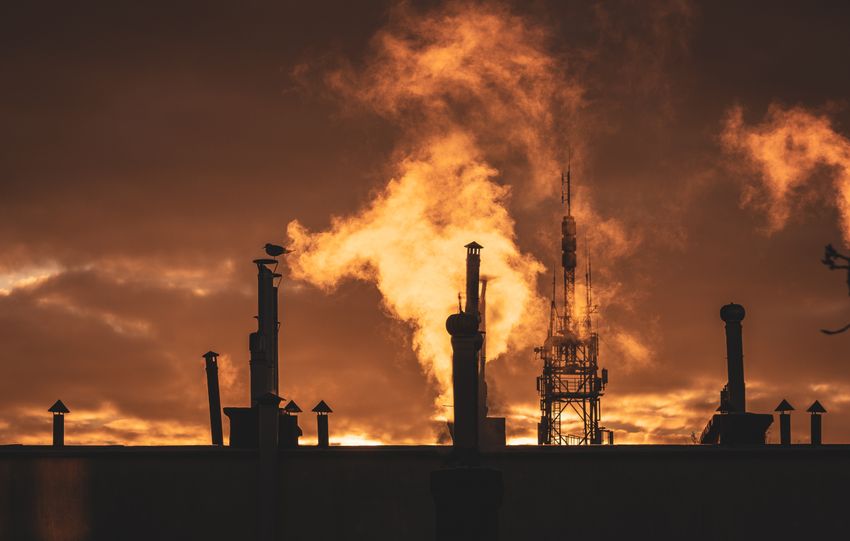Silhouette of industrial plant smokestacks against a dramatic sunset sky.