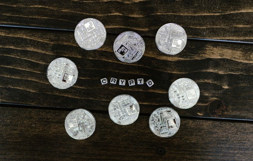 Silver cryptocurrency coins arranged on a wooden surface spelling 'crypto'.
