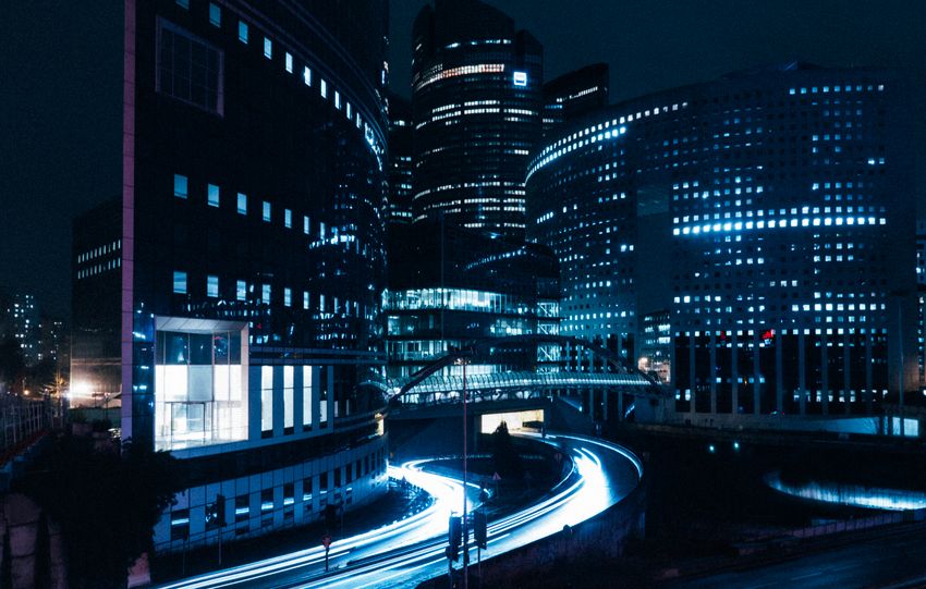 A stunning view of modern city buildings illuminated at night with dynamic light trails.