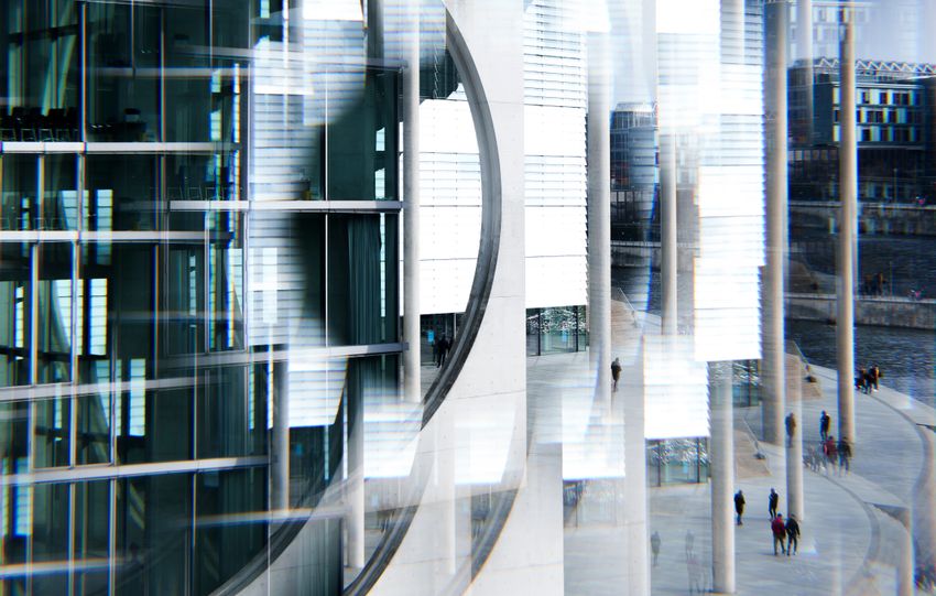 Abstract image capturing geometric reflections on a modern urban building with people walking nearby.