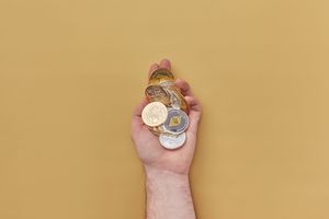 Close-up of a hand holding various cryptocurrency coins against a yellow background.