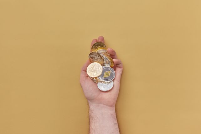 Close-up of a hand holding various cryptocurrency coins against a yellow background.