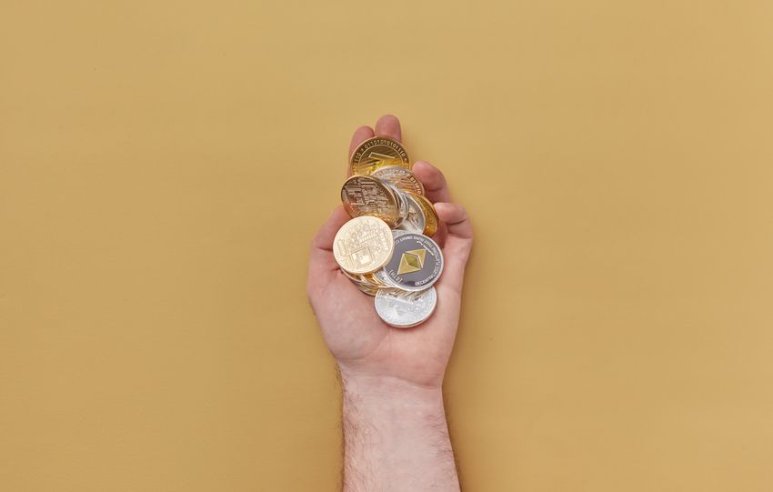 Close-up of a hand holding various cryptocurrency coins against a yellow background.
