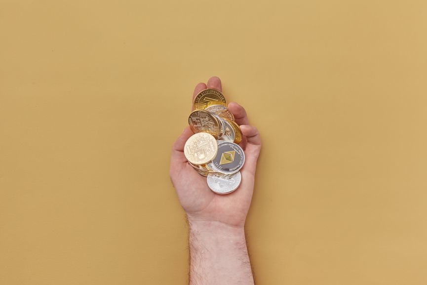 Close-up of a hand holding various cryptocurrency coins against a yellow background.