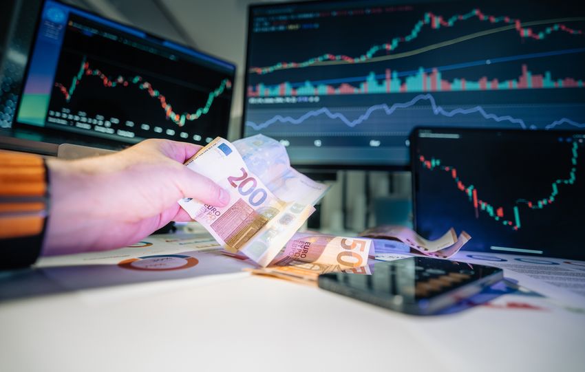 Close-up of euro banknotes with financial market graphs in the background, depicting finance and investment themes.