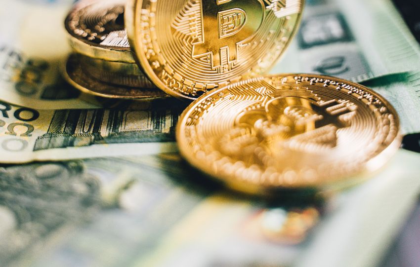 Close-up of golden Bitcoin coins on banknotes with a blurred cryptocurrency graph background.