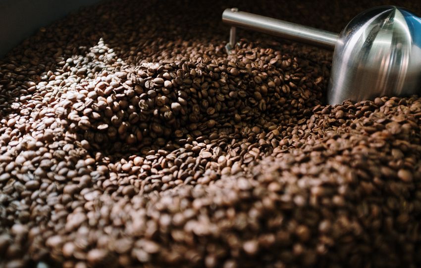 Detailed view of brown coffee beans being roasted in a steel machine, capturing the industrial process.