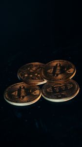 Four gold-colored Bitcoin coins arranged on a dark surface.