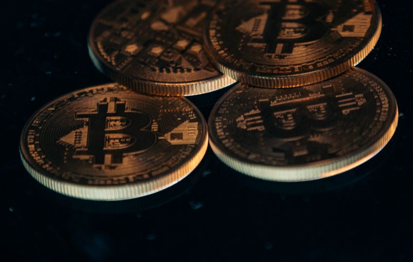Four gold-colored Bitcoin coins arranged on a dark surface.
