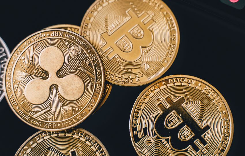 A detailed view of Bitcoin and Ripple coins with market data on a screen, symbolizing digital currency trends.