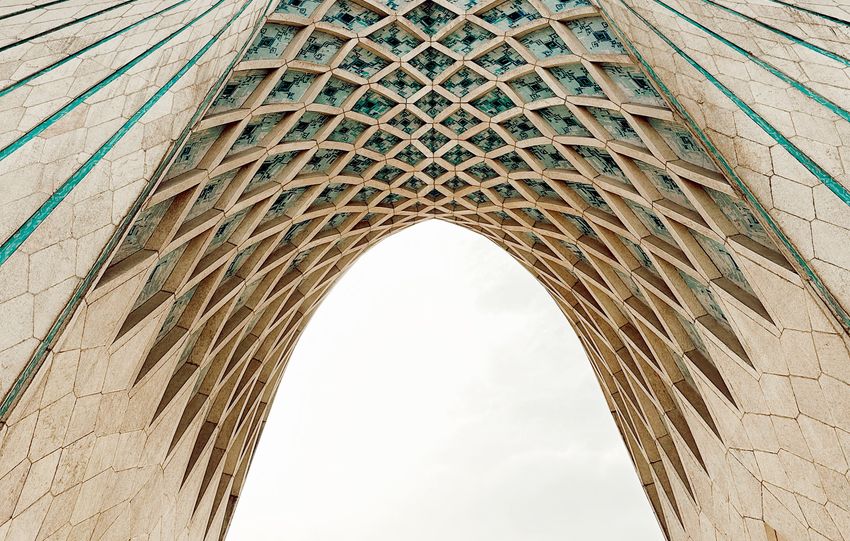 A dramatic upward shot of Azadi Tower against a blue sky in Tehran, Iran.