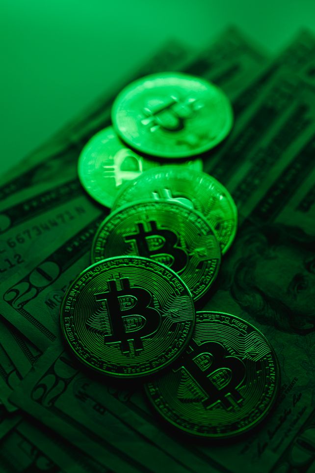 A stack of Bitcoin coins atop US dollar bills illuminated by green lighting, symbolizing digital finance and cryptocurrency.