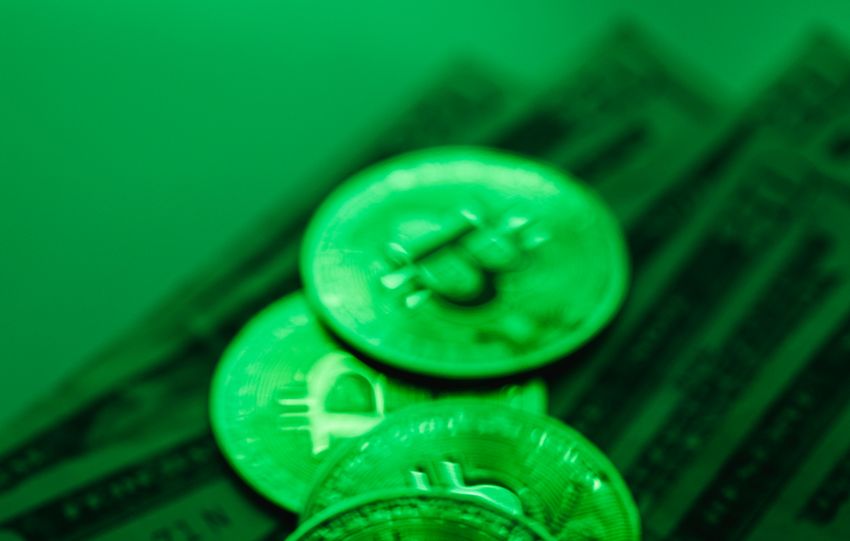A stack of Bitcoin coins atop US dollar bills illuminated by green lighting, symbolizing digital finance and cryptocurrency.