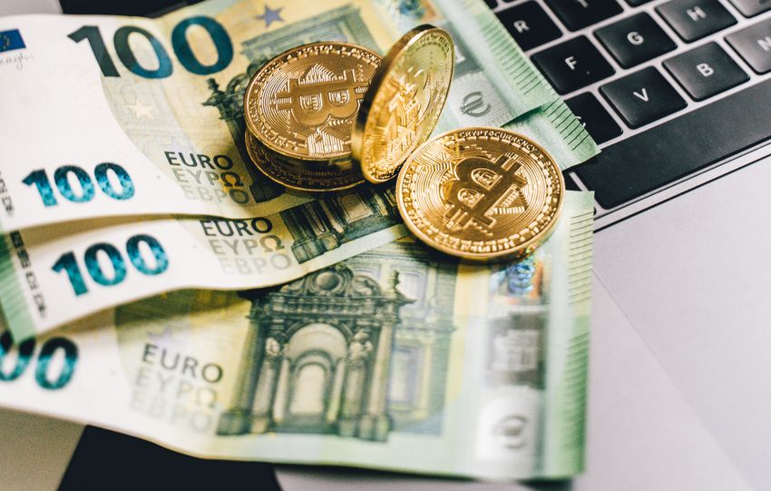Bitcoin and Euro notes on laptop keyboard with stock market graphs in Berlin, Germany.